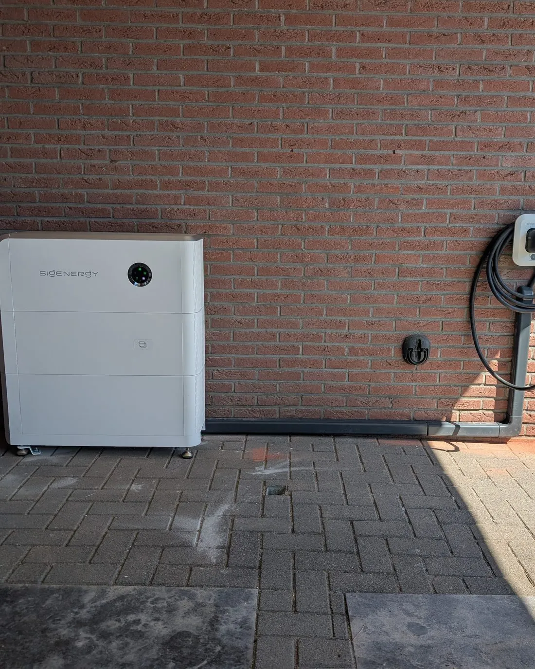 SigenStor buiten tegen de gevel, met een laadpaal ernaast